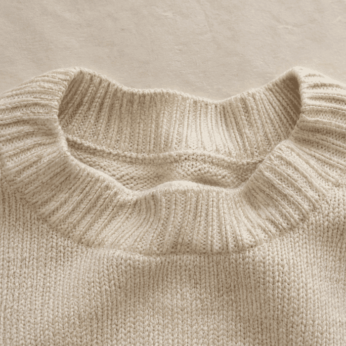 A stretched, wavy ribbed neckline on a cream knit sweater.